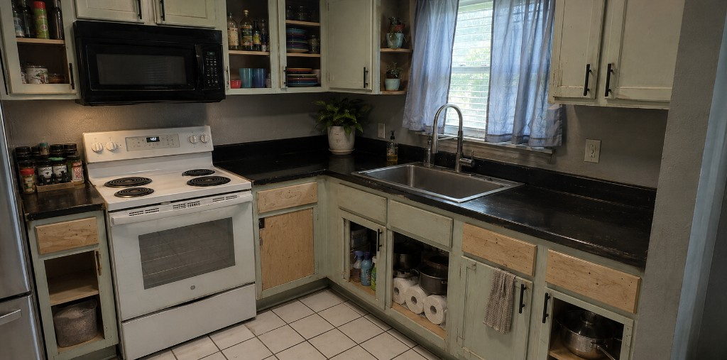 The same view before — black counters, dated tile flooring and tired cabinet fronts